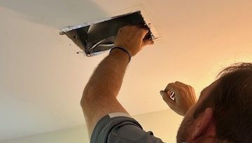 Air Duct Cleaning & Radon Co. technician thoroughly cleaning a removed air vent register with a specialized brush and vacuum