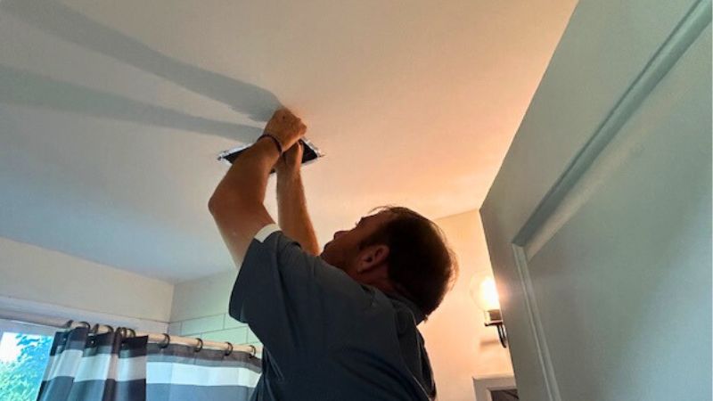 Close-up view of a technician using silver foil tape to seal the boot and air gaps around a white ceiling air register to prevent energy loss and dust infiltration.